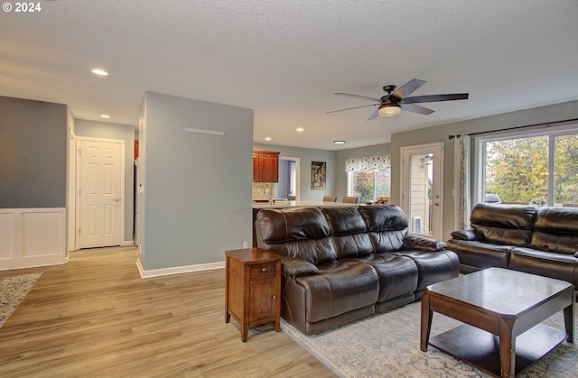 living room featuring light hardwood / wood-style floors, ceiling fan, and a textured ceiling