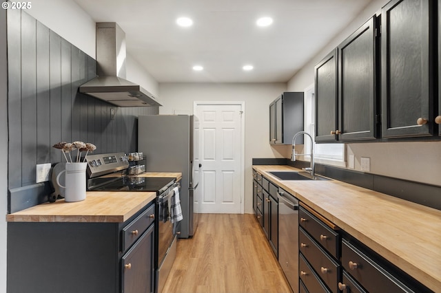 kitchen featuring sink, wall chimney exhaust hood, stainless steel appliances, butcher block countertops, and light wood-type flooring