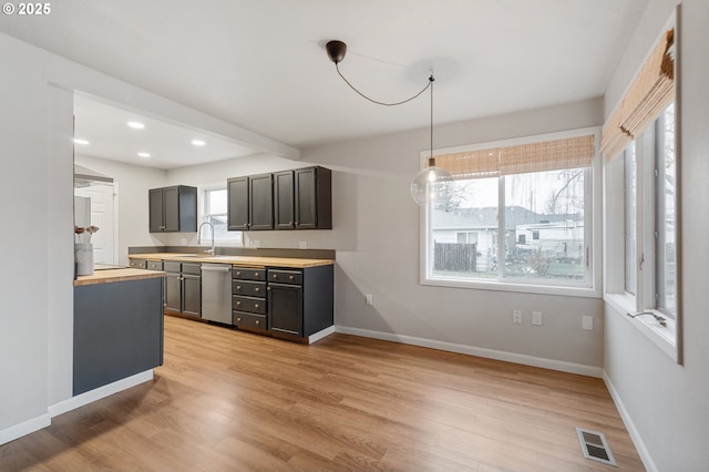 kitchen featuring wooden counters, stainless steel dishwasher, sink, decorative light fixtures, and light hardwood / wood-style floors