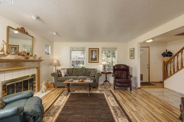 living room with light wood-type flooring, a textured ceiling, and a tile fireplace