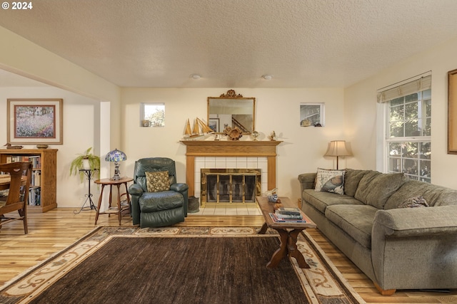 living room featuring a tile fireplace, plenty of natural light, light hardwood / wood-style floors, and a textured ceiling