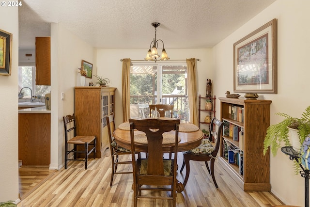 dining area with a textured ceiling, an inviting chandelier, sink, and light hardwood / wood-style floors