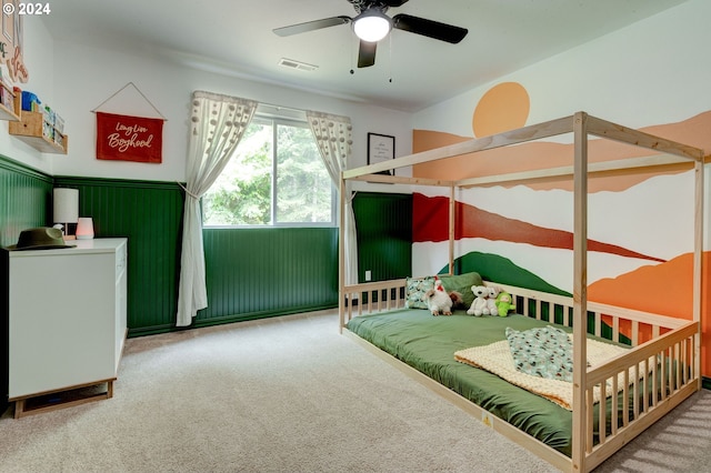 carpeted bedroom with a wainscoted wall, visible vents, and a ceiling fan