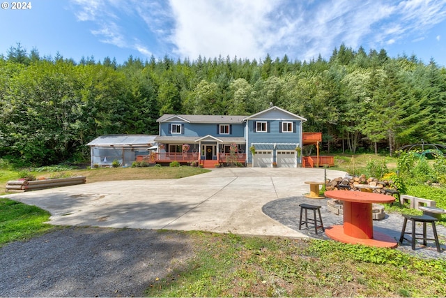 view of front of home featuring a garage, driveway, a forest view, and a porch