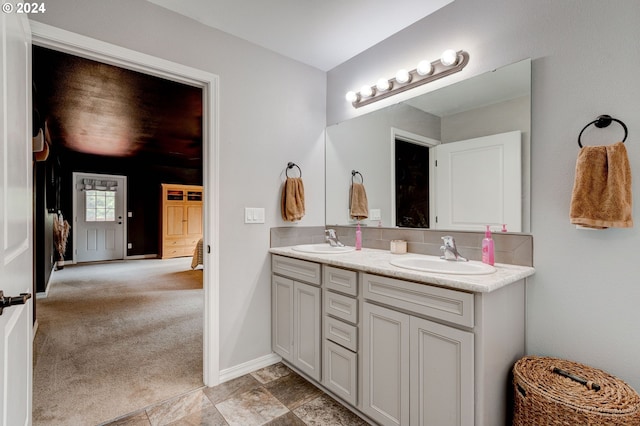 ensuite bathroom with double vanity, connected bathroom, baseboards, and a sink