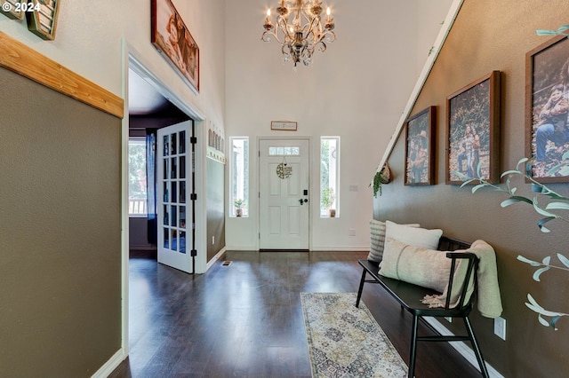 entrance foyer with dark wood-style flooring, a towering ceiling, baseboards, and an inviting chandelier