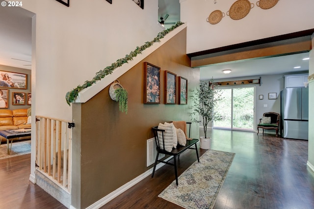 hallway with a high ceiling, dark wood finished floors, visible vents, and baseboards