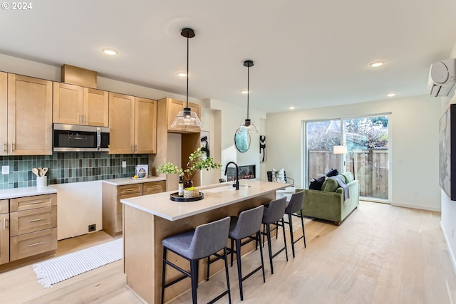 kitchen with a wall mounted air conditioner, light brown cabinets, decorative backsplash, an island with sink, and decorative light fixtures