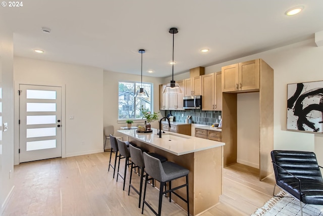 kitchen featuring decorative backsplash, light wood-type flooring, sink, a center island with sink, and hanging light fixtures