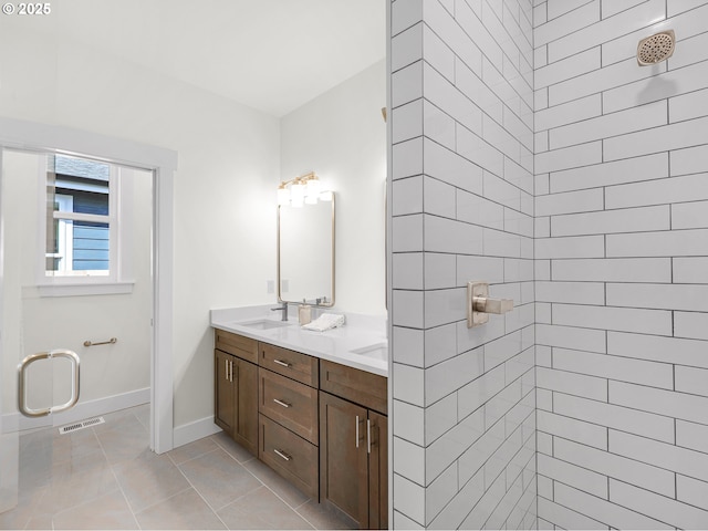 bathroom with a sink, double vanity, tiled shower, baseboards, and visible vents