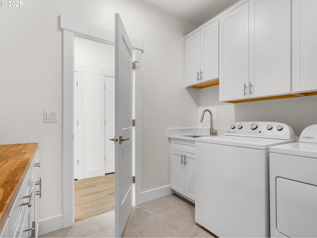 laundry area featuring a sink, baseboards, separate washer and dryer, cabinet space, and light tile patterned floors