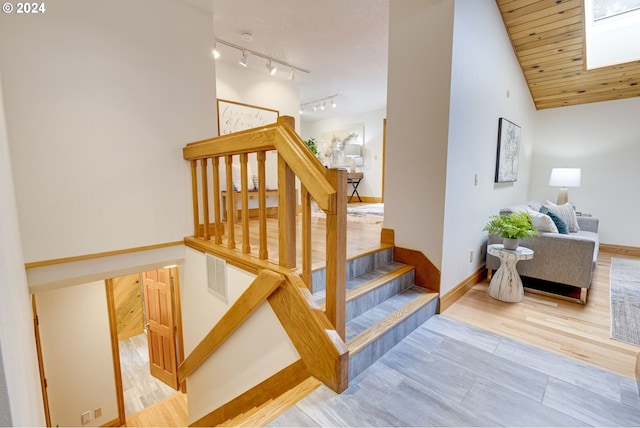 stairs with track lighting, hardwood / wood-style floors, and lofted ceiling with skylight