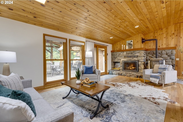 living room with wood ceiling, lofted ceiling, a stone fireplace, and light hardwood / wood-style floors