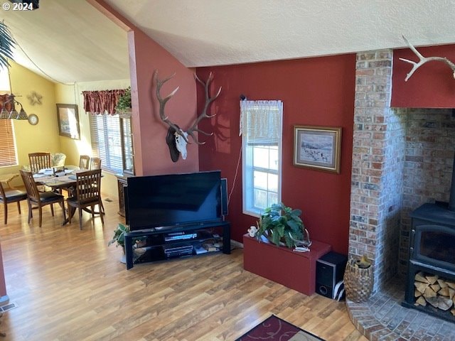 living room featuring lofted ceiling, wood-type flooring, a healthy amount of sunlight, and a wood stove