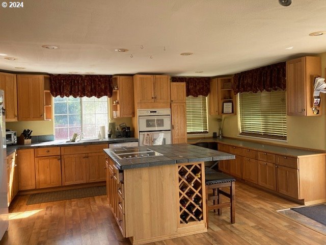 kitchen featuring a kitchen island, stainless steel gas stovetop, double oven, wood-type flooring, and sink