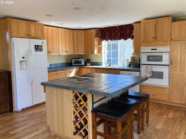 kitchen featuring a breakfast bar, white appliances, tile countertops, and light hardwood / wood-style flooring