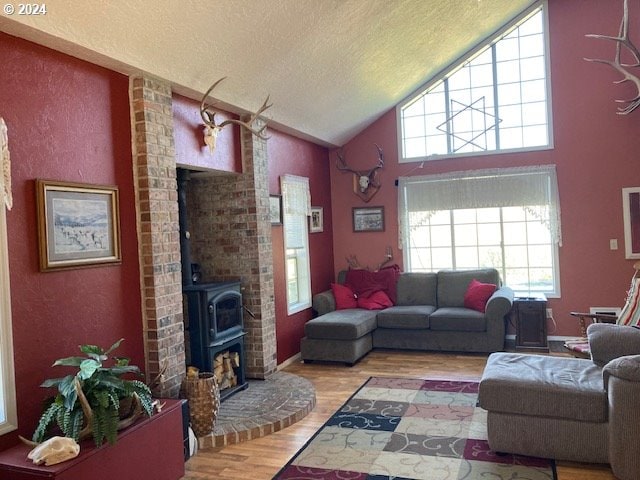 living room featuring a textured ceiling, light hardwood / wood-style flooring, high vaulted ceiling, and a wood stove