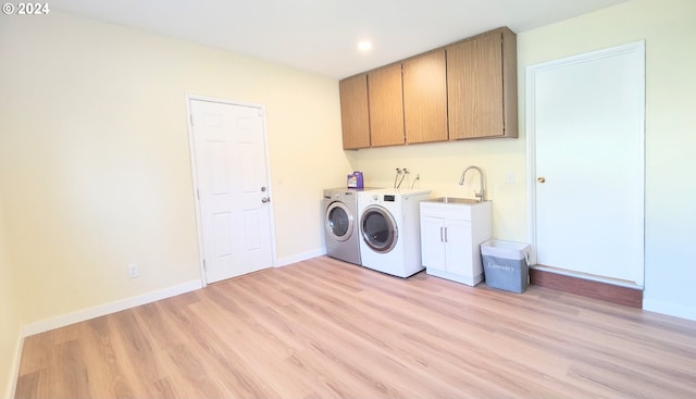 clothes washing area with sink, cabinets, light hardwood / wood-style flooring, and washing machine and clothes dryer