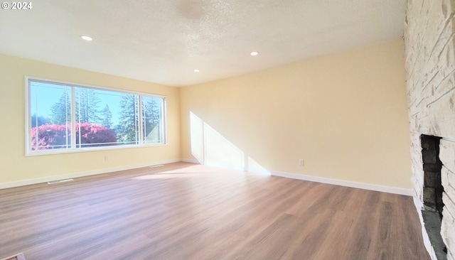 unfurnished living room featuring a textured ceiling, light wood-type flooring, and a stone fireplace