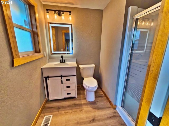 bathroom with toilet, wood-type flooring, vanity, and a shower with door