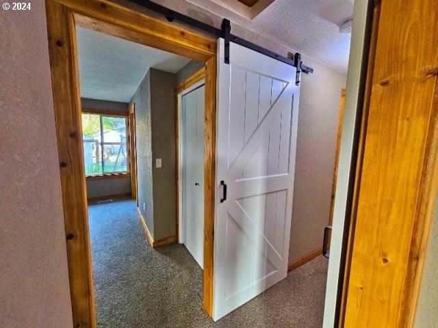 hall featuring a textured ceiling, carpet, and a barn door