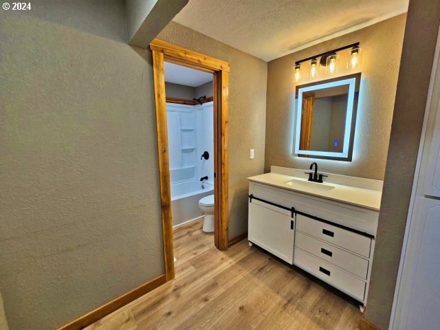 full bathroom with a textured ceiling, wood-type flooring, vanity, shower / bath combination, and toilet