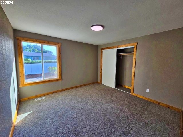 unfurnished bedroom featuring a closet, a water view, a textured ceiling, and carpet