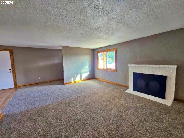 unfurnished living room featuring a fireplace, carpet floors, and a textured ceiling