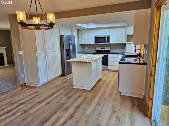 kitchen with white cabinets, a kitchen island, pendant lighting, light wood-type flooring, and appliances with stainless steel finishes