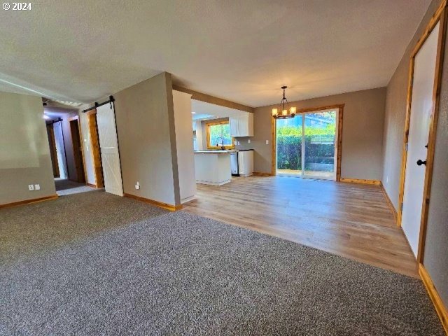 unfurnished living room with a barn door, a chandelier, a textured ceiling, and light hardwood / wood-style flooring