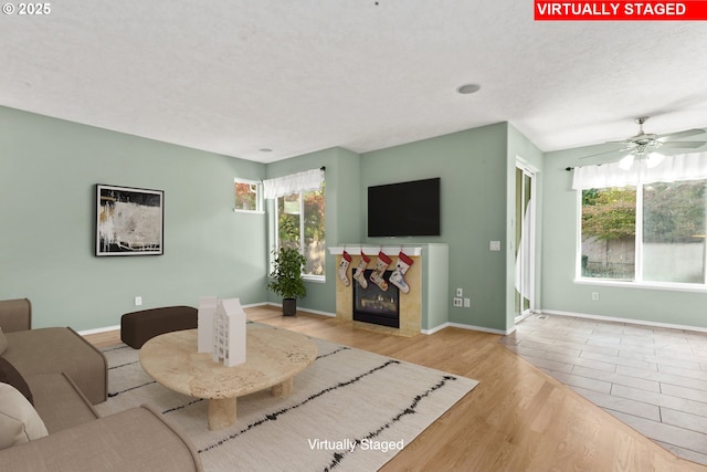 living room with a premium fireplace, a wealth of natural light, ceiling fan, and light hardwood / wood-style floors