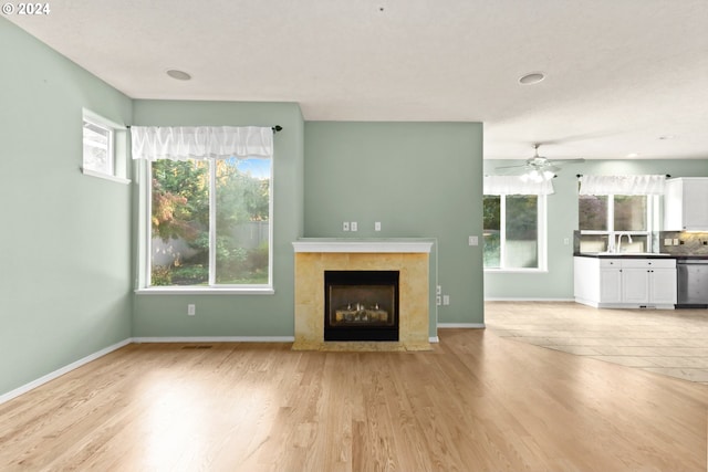 unfurnished living room with a tile fireplace, light hardwood / wood-style flooring, plenty of natural light, and sink