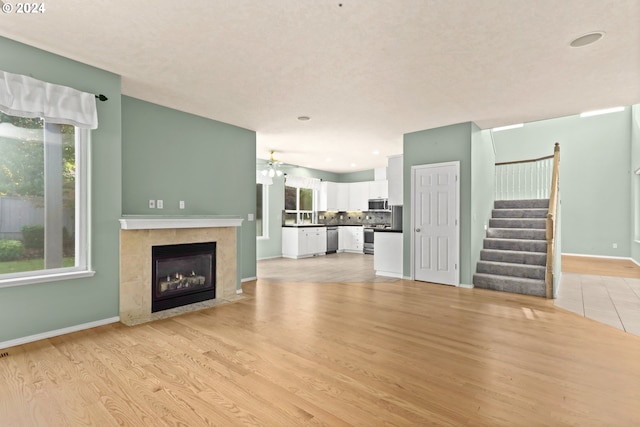 unfurnished living room featuring a tile fireplace, ceiling fan, and light hardwood / wood-style floors