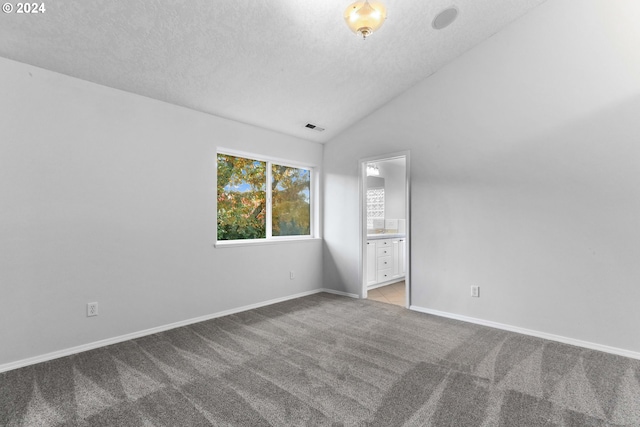 unfurnished bedroom with a textured ceiling, vaulted ceiling, light colored carpet, and ensuite bath