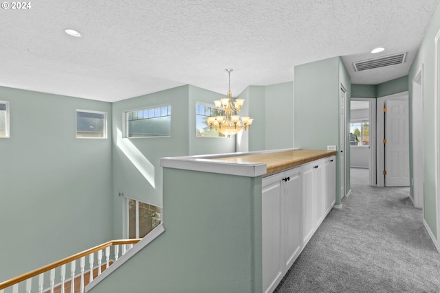 hall featuring plenty of natural light, light colored carpet, a textured ceiling, and an inviting chandelier