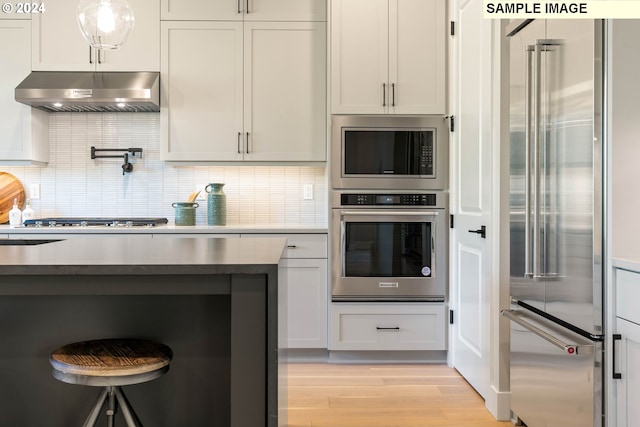 kitchen with white cabinetry, stainless steel appliances, light hardwood / wood-style flooring, extractor fan, and decorative backsplash