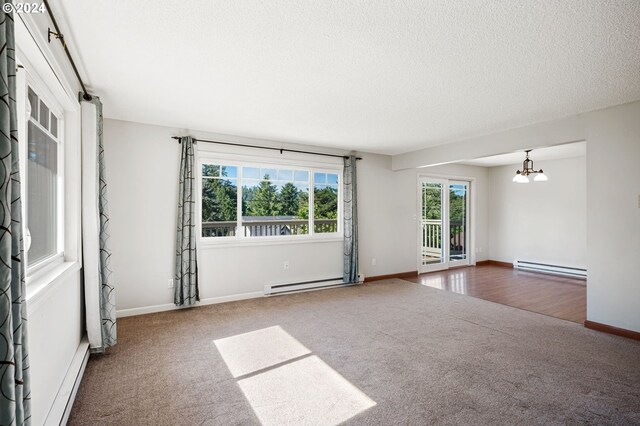 carpeted empty room featuring a textured ceiling, a baseboard heating unit, and a chandelier