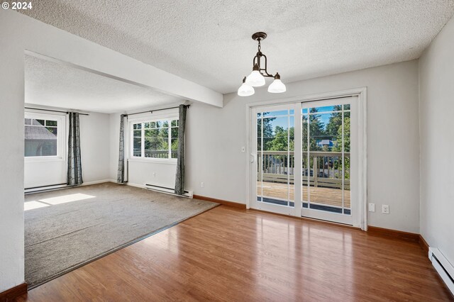 spare room with a healthy amount of sunlight, baseboard heating, wood-type flooring, and a chandelier