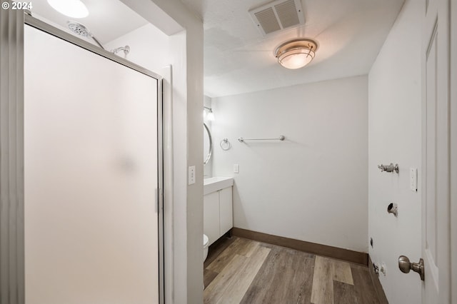 bathroom featuring hardwood / wood-style flooring, a shower with shower door, toilet, and vanity