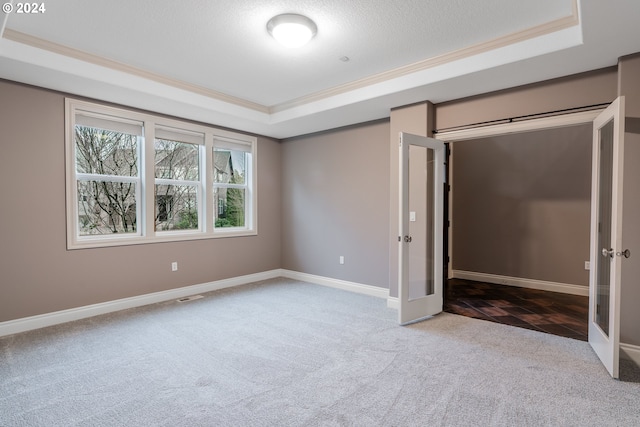 unfurnished bedroom featuring a tray ceiling, crown molding, french doors, and carpet