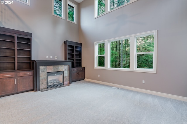 unfurnished living room with light carpet, a high ceiling, and a tile fireplace