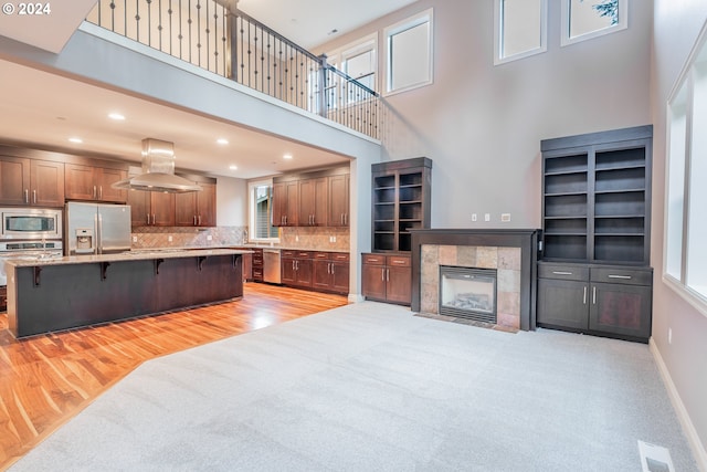 living room with beverage cooler, a tiled fireplace, a high ceiling, and light hardwood / wood-style flooring