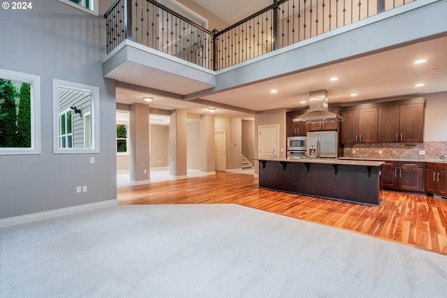 kitchen featuring island exhaust hood, appliances with stainless steel finishes, a towering ceiling, light hardwood / wood-style flooring, and a breakfast bar area