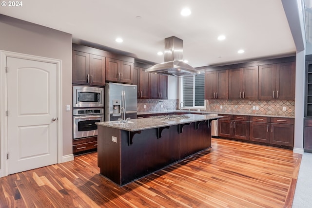 kitchen featuring light stone countertops, a kitchen island, a kitchen bar, island exhaust hood, and stainless steel appliances