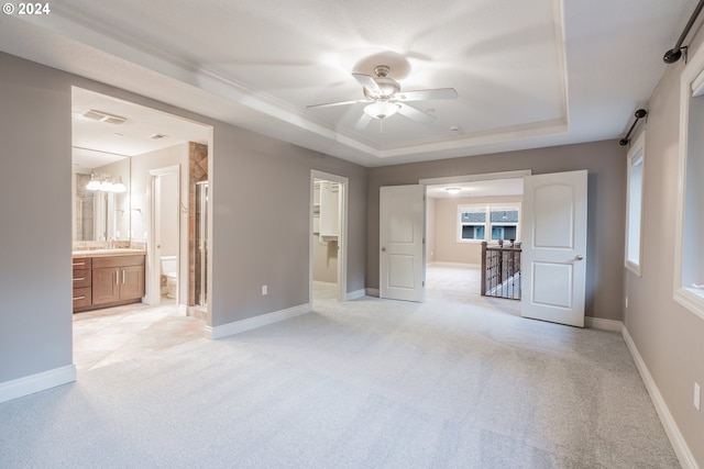 unfurnished bedroom with ceiling fan with notable chandelier, light colored carpet, a raised ceiling, and ensuite bathroom