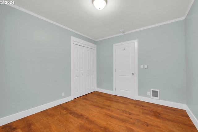 unfurnished bedroom with wood-type flooring, ornamental molding, and a closet