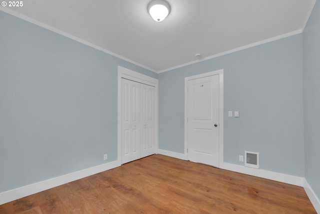 empty room with wood finished floors, visible vents, baseboards, and ornamental molding