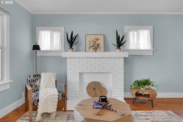 sitting room with baseboards, ornamental molding, a brick fireplace, and wood finished floors