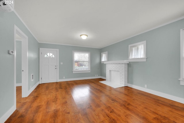 entrance foyer with wood-type flooring, ornamental molding, and a brick fireplace