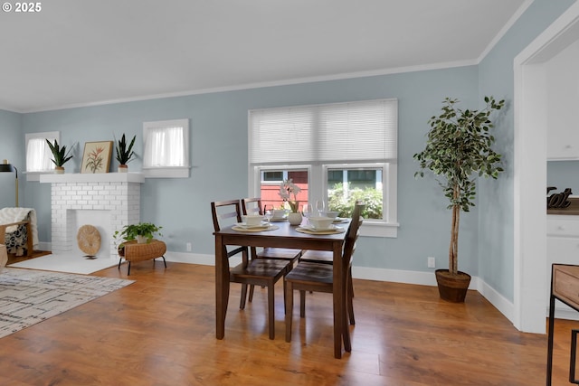 dining area with baseboards, ornamental molding, wood finished floors, and a fireplace